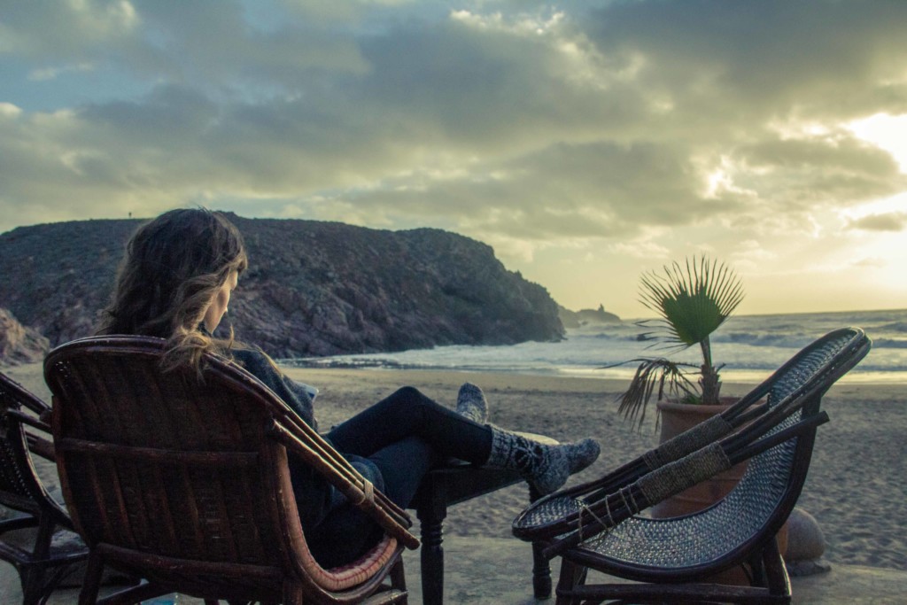 Mariana looking at her phone with a beach sunset in front of her in Mirleft